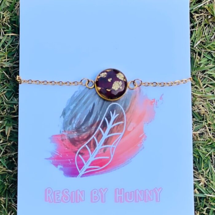 Heart-shaped resin bracelet with preserved flowers and a golden chain, placed on a white fabric background with blue flowers.
